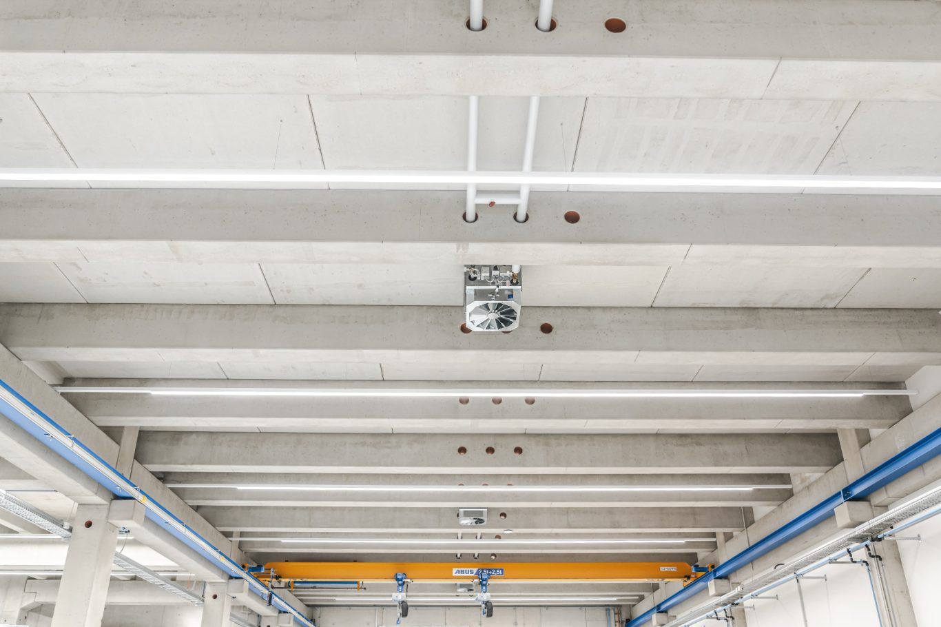 Hallenbeleuchtung Decke eines Industriegebäudes mit sichtbaren Rohren und elektrischen Leitungen.