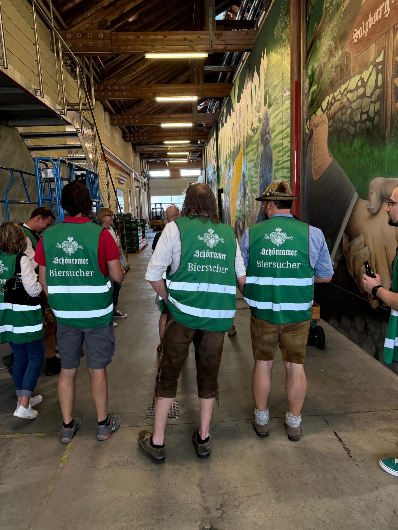 Gruppierung von Personen in grünen Westen in einer Lagerhalle mit Wandmalerei.
