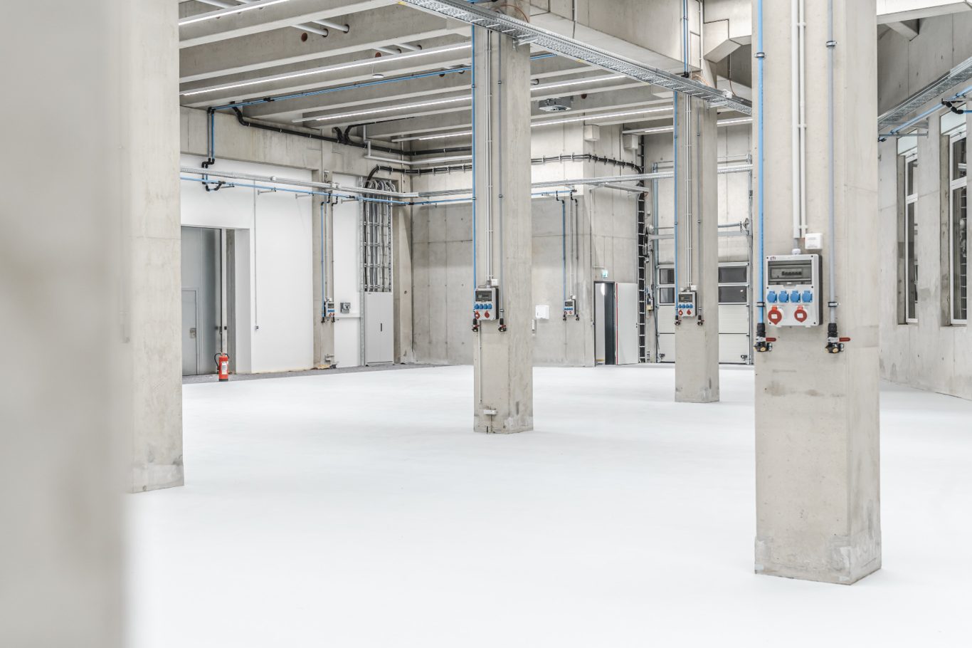 Produktionshalle Leere, helle Lagerhalle mit Betonstützen und weißen Böden.