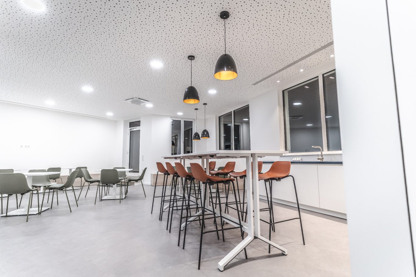 Kantine Moderner Bereich mit Barhockern und Tischen, helle Wände und Deckenlampen.