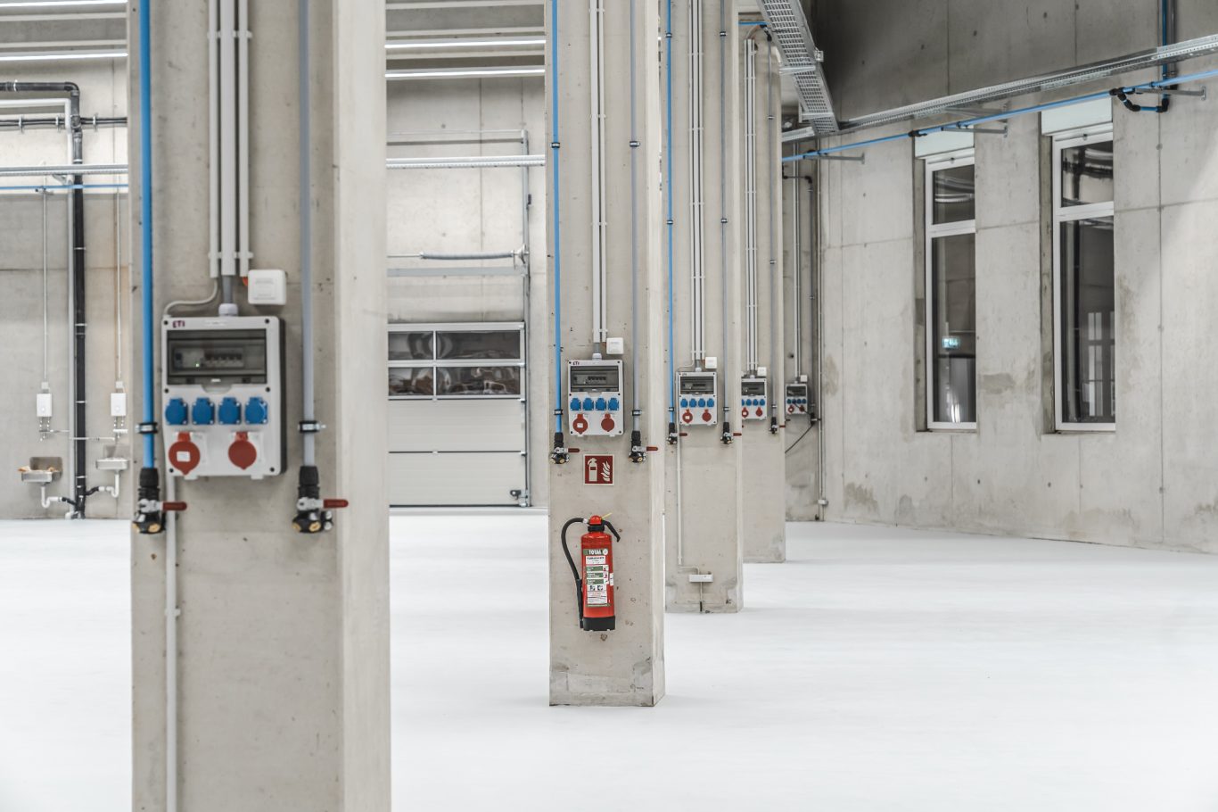CEE-Verteiler Helle Industriehalle mit Säulen, Kontrollpanels und Feuerlöscher an den Wänden.