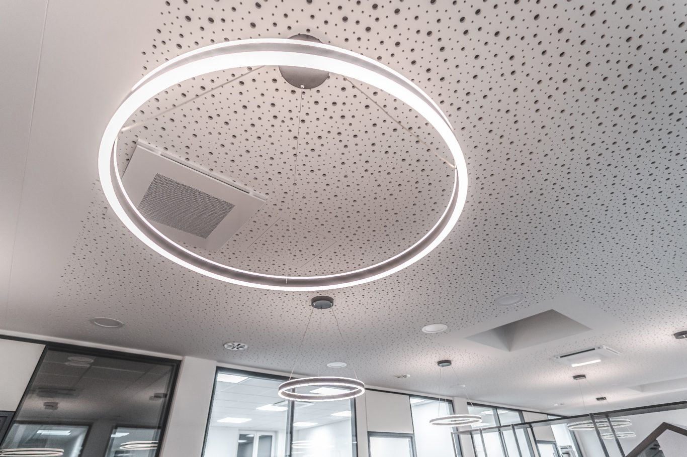 Beleuchtungssystem Bürovorraum Moderne Deckenleuchte in einem eleganten, hellen Raum mit akustischen Paneelen.